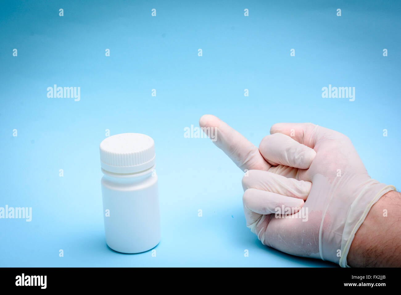 Mano nel guanto di medici e bottiglia bianca su sfondo blu Foto Stock