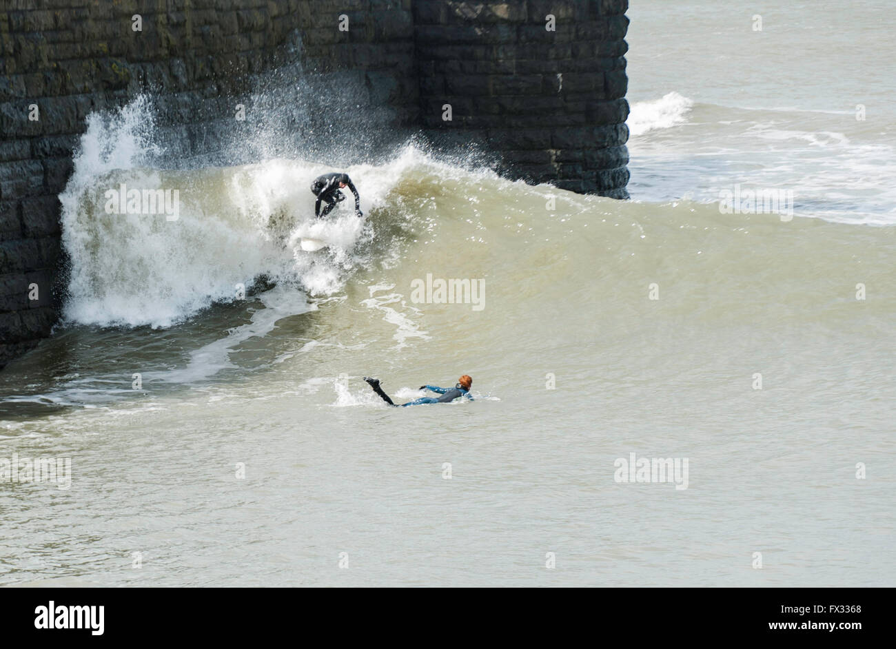 Aberystwyth, Ceredigion, West Wales, 10 aprile 2016 UK Meteo: Due Surfers prendere vantaggio della maggiore rispetto al normale alta marea a 5.48m, l'aumento di vento e la massiccia gonfiarsi per navigare pericolosamente vicino lungo la banchina a parete come la gente guarda a scattare foto e video godendo il vento ancora chiaro meteo. Credito: Veterano Fotografia/Alamy Live News Foto Stock