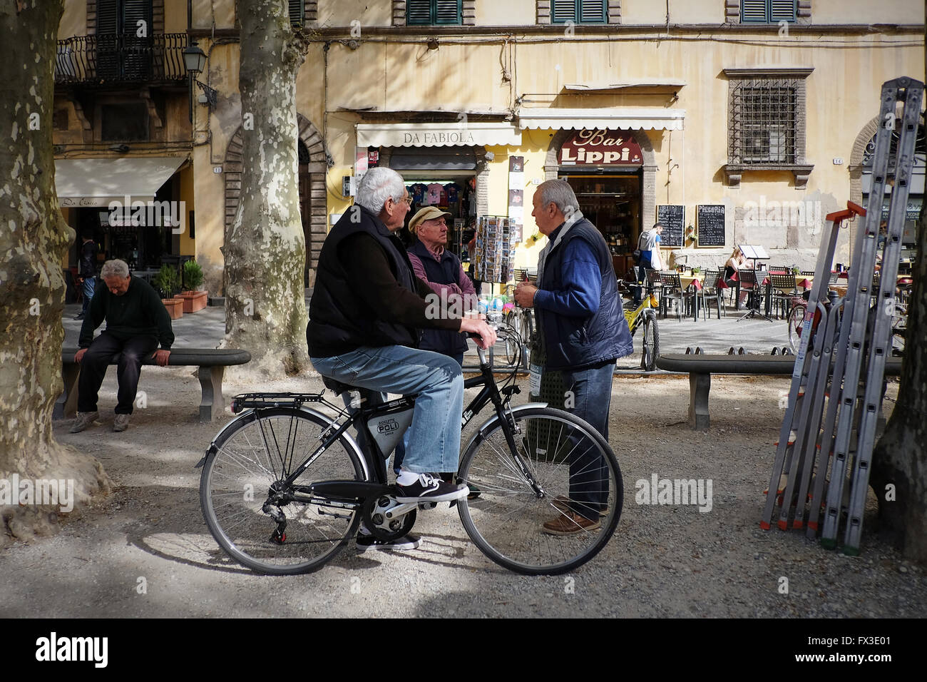 Tre vecchi uomini italiani uno su una bicicletta, parlare in pezzata dalla  luce del sole al di fuori di un negozio Foto stock - Alamy