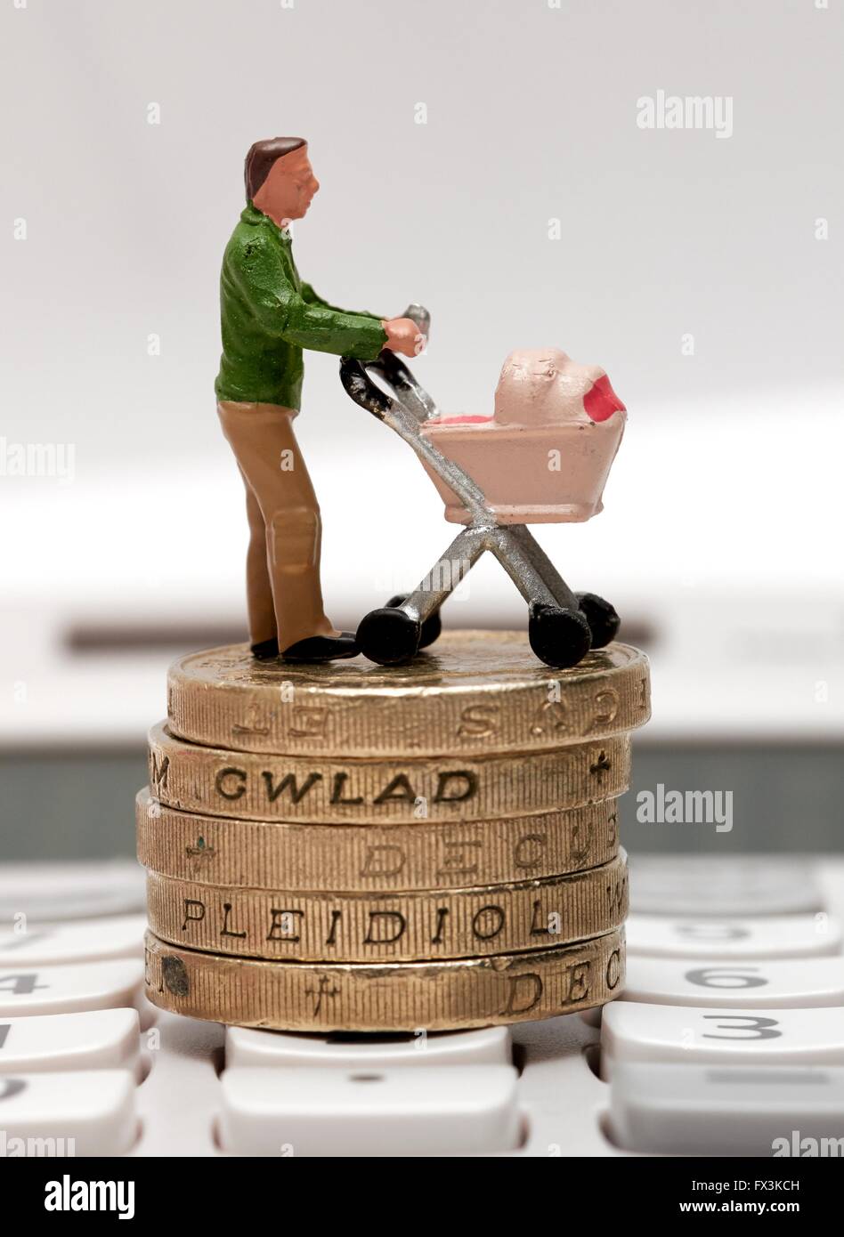 Un unico maschio statuetta in miniatura genitore con una carrozzina permanente sulla libbra di monete e di una calcolatrice Foto Stock
