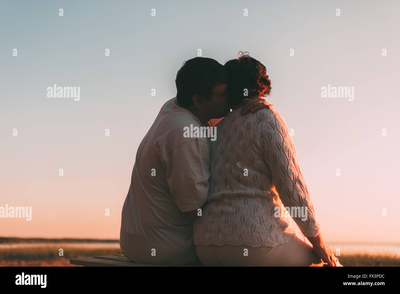 Vista posteriore di una coppia sposata una silhouette seduta su una panchina. Foto Stock