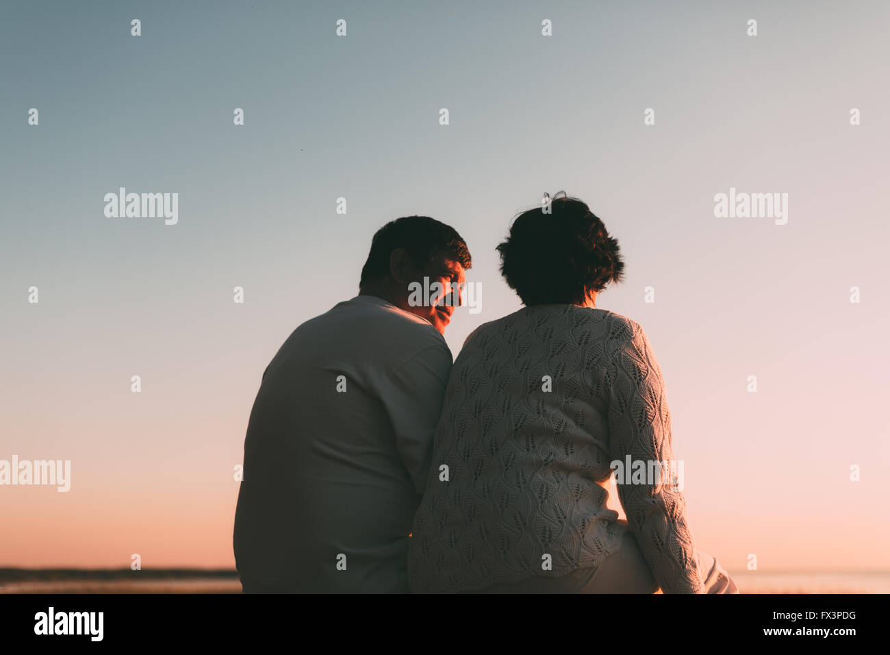 Vista posteriore di una coppia sposata una silhouette seduta su una panchina. Foto Stock