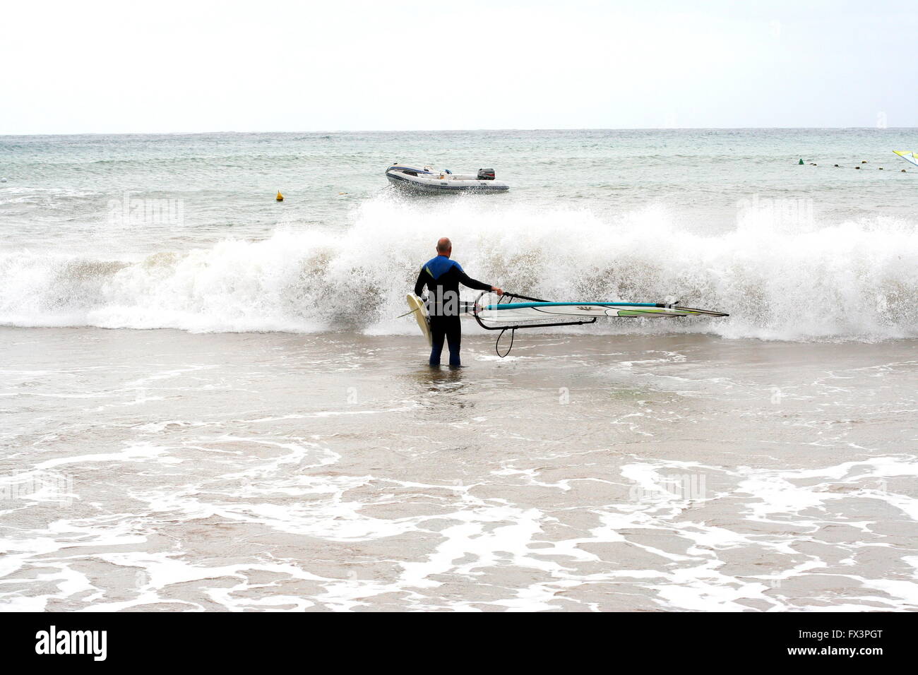 Un uomo che porta la sua tavola da surf in acqua per praticare windsurf, wind surf presso la spiaggia di Costa Teguise Lanzarote, Spagna, onde schiumose concept Foto Stock