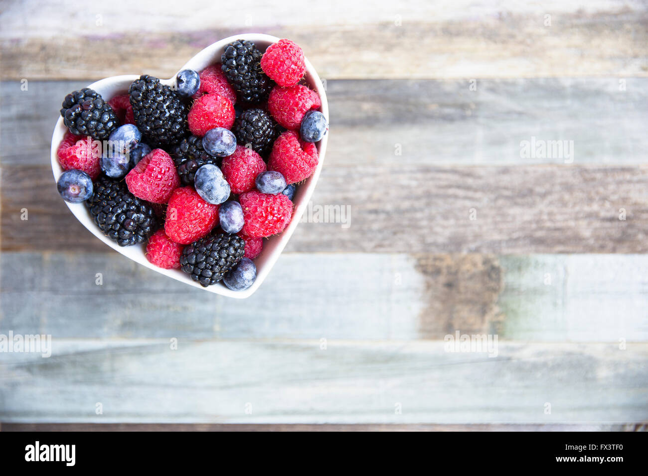 Una sana frutta fresca insalata di fragole, more, mirtilli e lamponi. in forma di cuore ciotola. Foto Stock