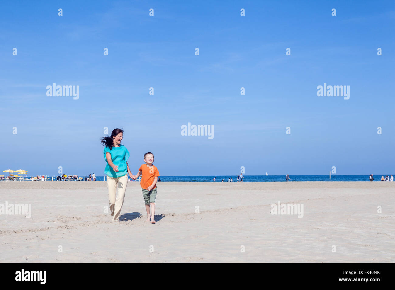 Mamma e suo figlio in esecuzione sulla spiaggia in un giorno di estate sul mare Adriatico in Italia, Marina di Ravenna Foto Stock