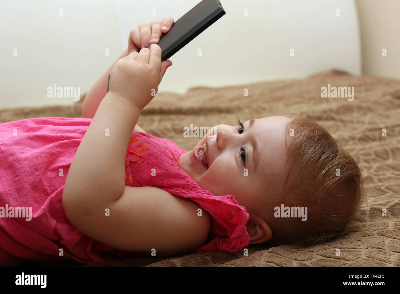 Poco sorridente bambino che gioca con lo smartphone giacente su un divano Foto Stock
