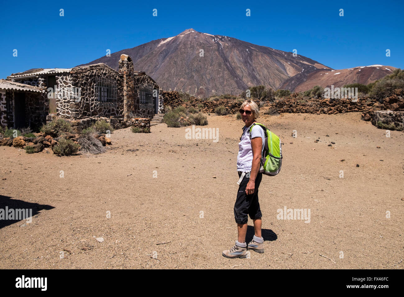 Donna anziana a piedi in Las Canadas del Teide national park, al sanatorio di vecchi edifici con il Teide in background, Te Foto Stock