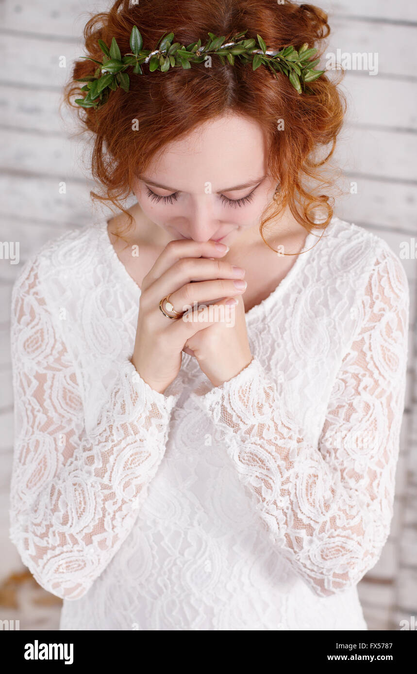 I giovani i capelli rossi sposa in una verde ghirlanda sorridendo delicatamente, le mani giunte in preghiera. Foto Stock