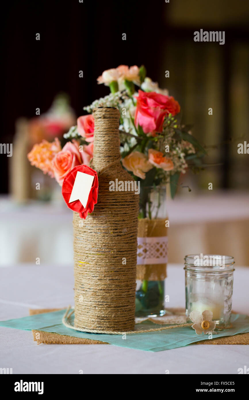 Per il FAI DA TE decorazioni per matrimoni centritavola tavola con bottiglie di vino avvolto in tela ruvida di spago e rose fiori. Foto Stock