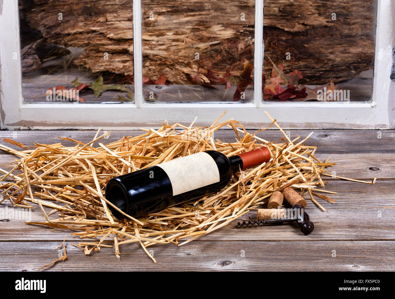 Una bottiglia di vino sulla paglia con la vecchia vite di sughero su rustiche in legno e vetro in background. Foto Stock