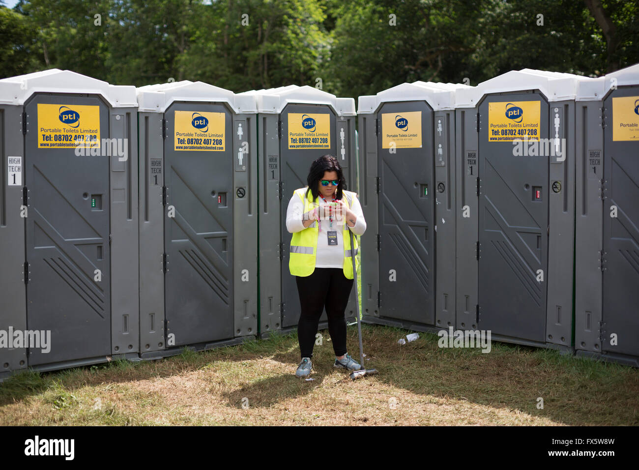 Womad Festival, Wiltshire e un wc attendent guardando lei mobiel phone. Foto Stock
