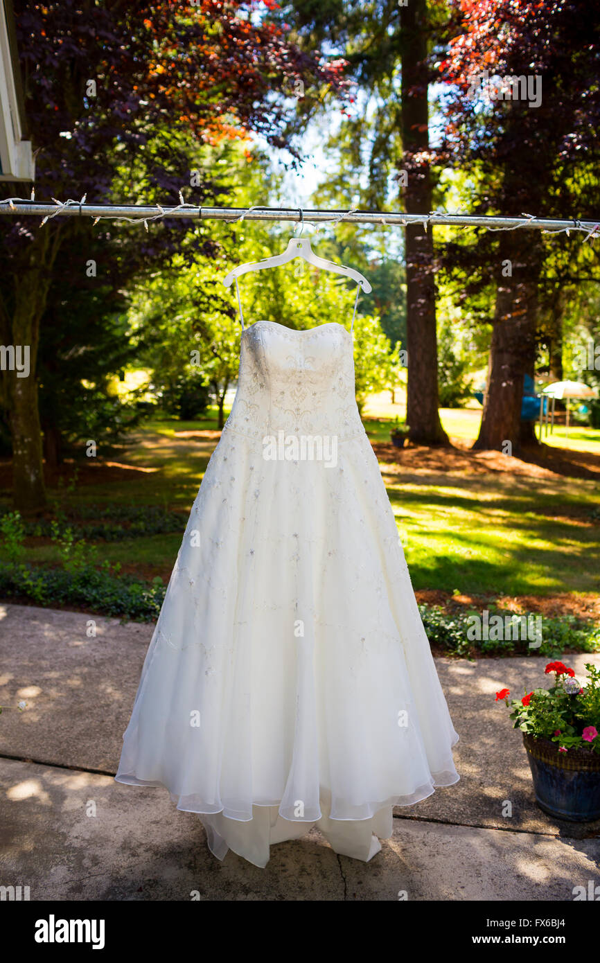 White abito da sposa appeso all'aperto da alcune luci. Foto Stock