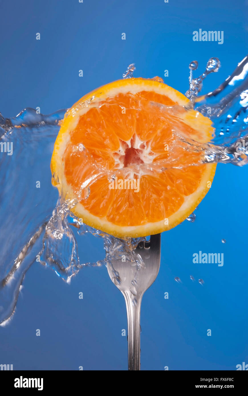 Frutta di arancia mezza sulla forcella con acqua splash e vuoto sfondo blu. Concetto di salute foto, ideale per poster o di campagna. Foto Stock