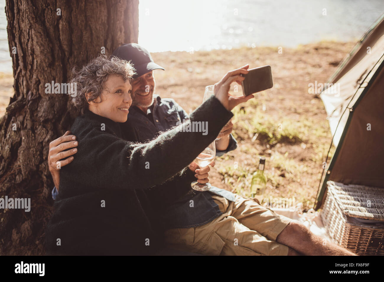 Scatto di una coppia senior di scattare una foto di loro stessi mentre si trova al di fuori di una tenda. Coppia matura campeggio vicino a un lago prendendo un selfie wit Foto Stock