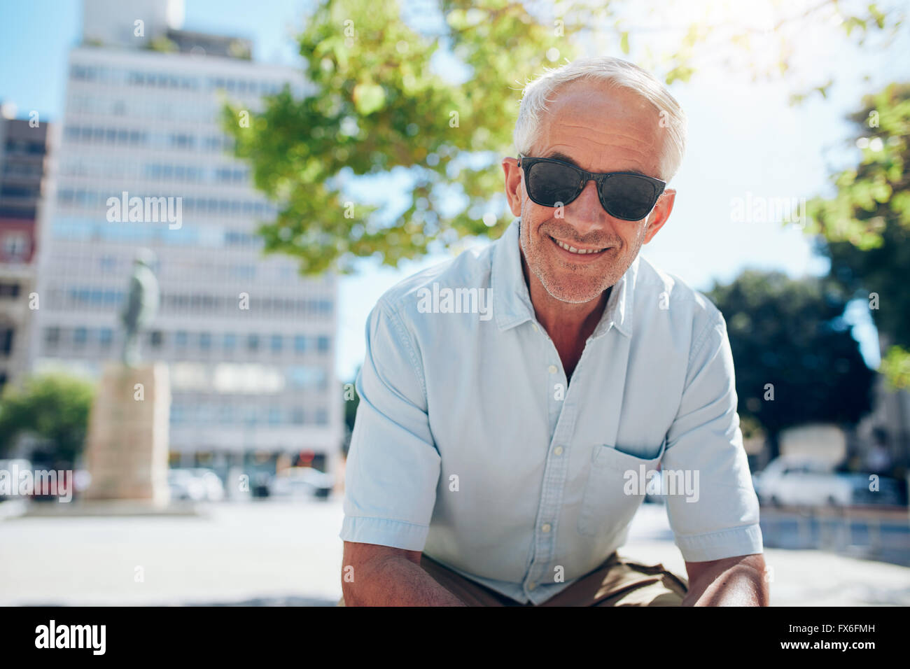 Ritratto di felice senior uomo seduto al di fuori della città. Uomo maturo con occhiali da sole all'aperto su un giorno d'estate. Foto Stock