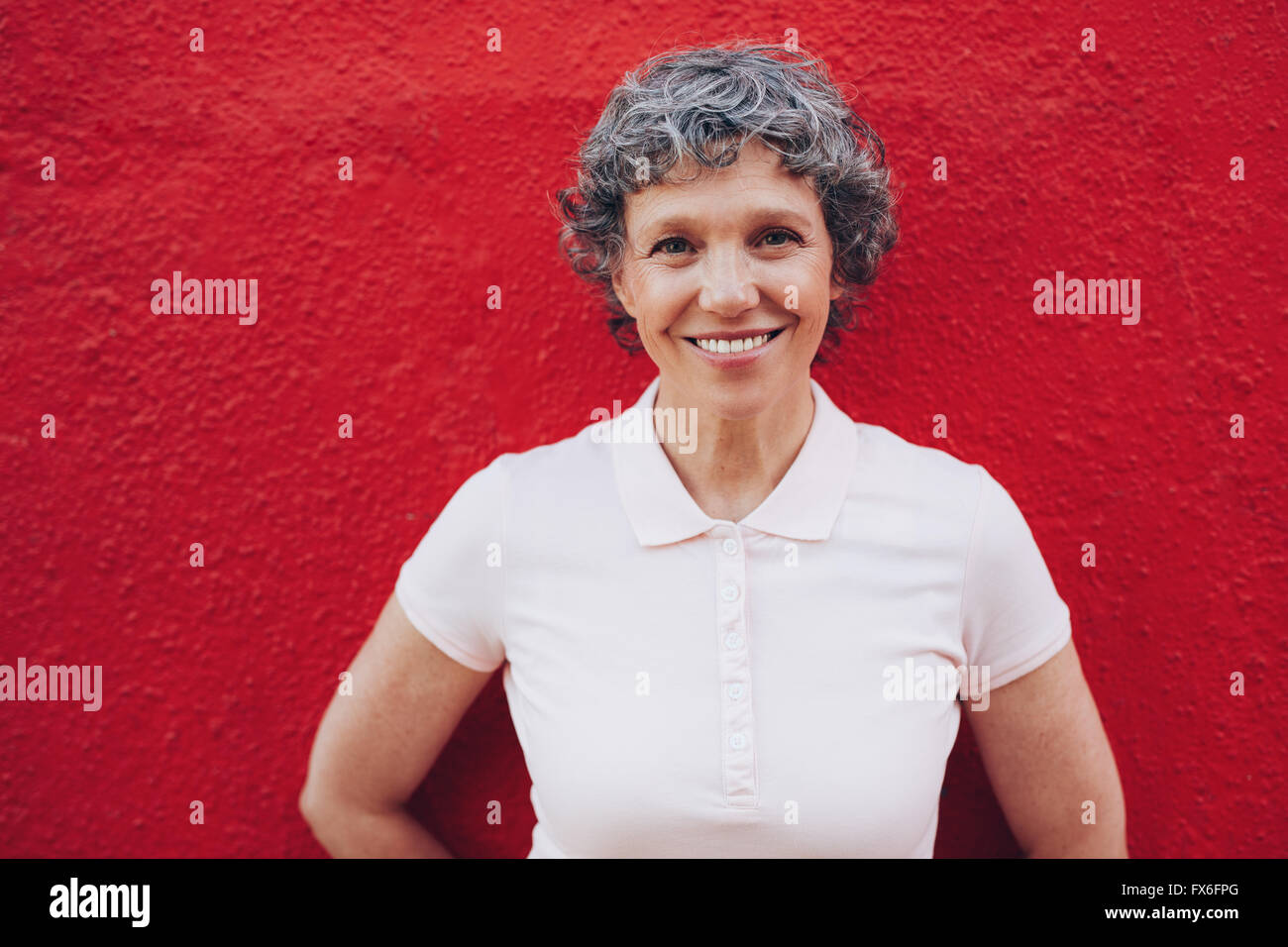 Ritratto di donna senior in piedi contro lo sfondo di colore rosso. Sorridente metà femmina adulta contro la parete rossa. Foto Stock