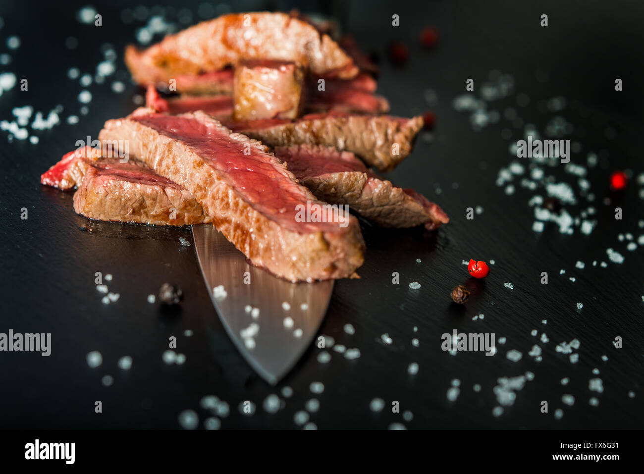 Raro medie fette di bistecca su un coltello sulla piastra nera, con scaglie di sale e di pepe Foto Stock