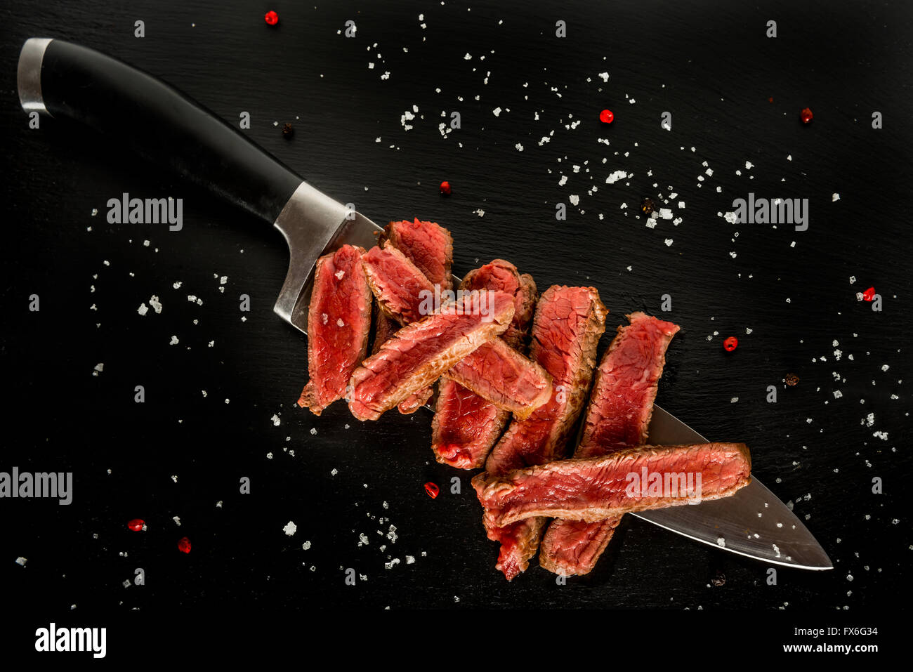 Raro medie fette di bistecca su un coltello sulla piastra nera, con scaglie di sale e di pepe Foto Stock