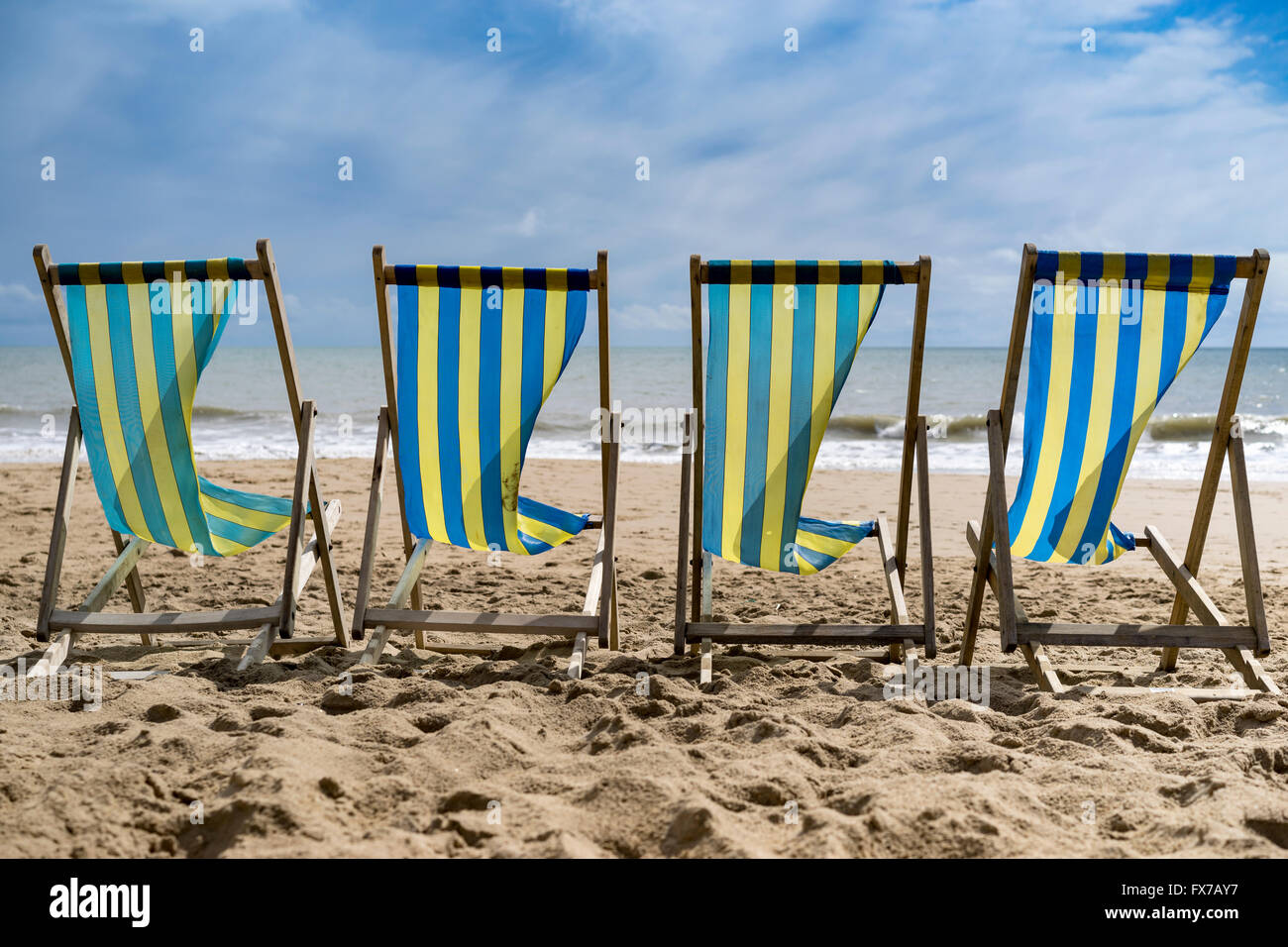 Una fila di 4 blu e giallo listati di sedie a sdraio al vento sulla spiaggia di Bournemouth, Regno Unito Foto Stock
