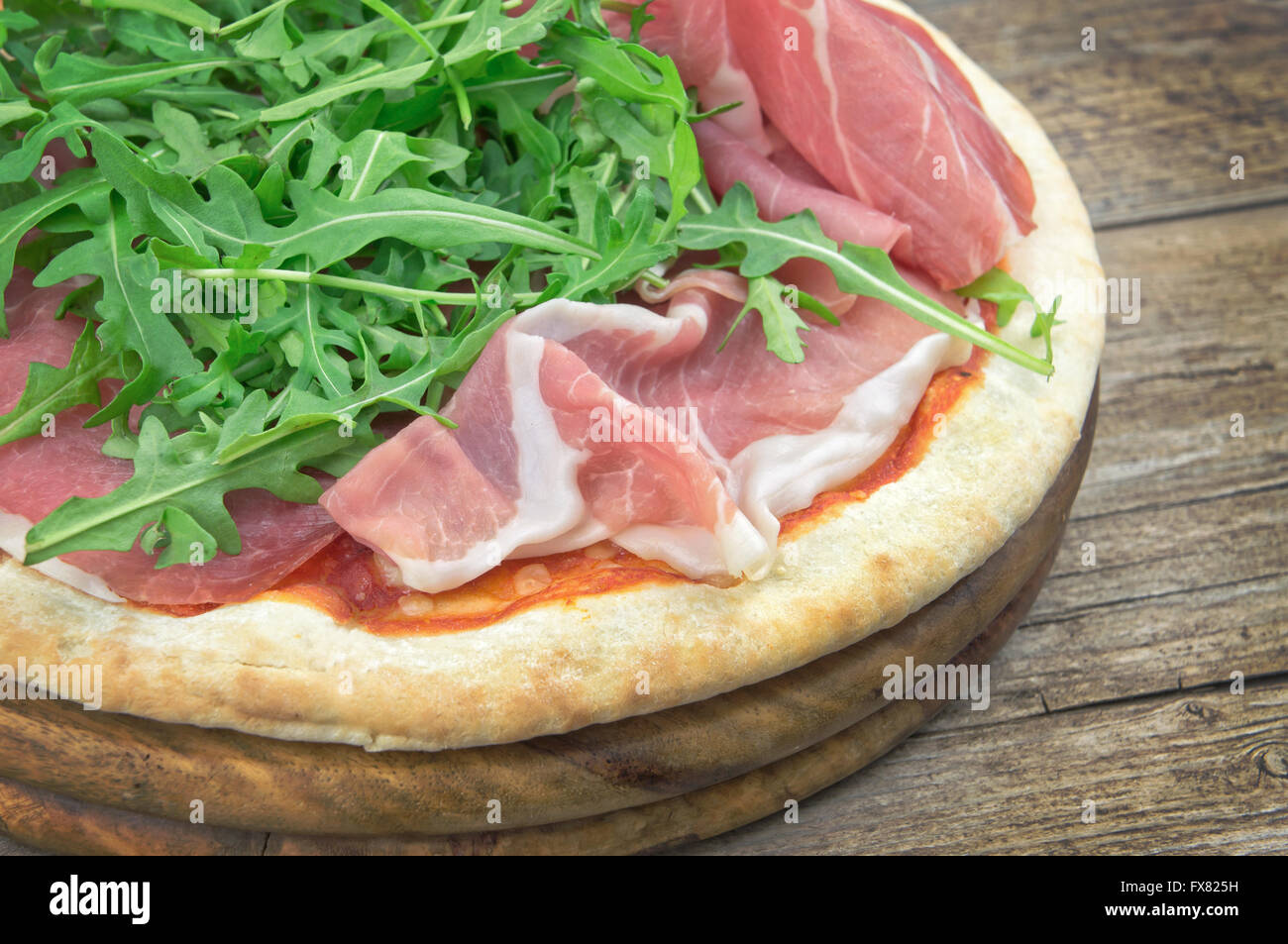 Pizza con insalata di rucola e prosciutto su piatto di legno Foto Stock