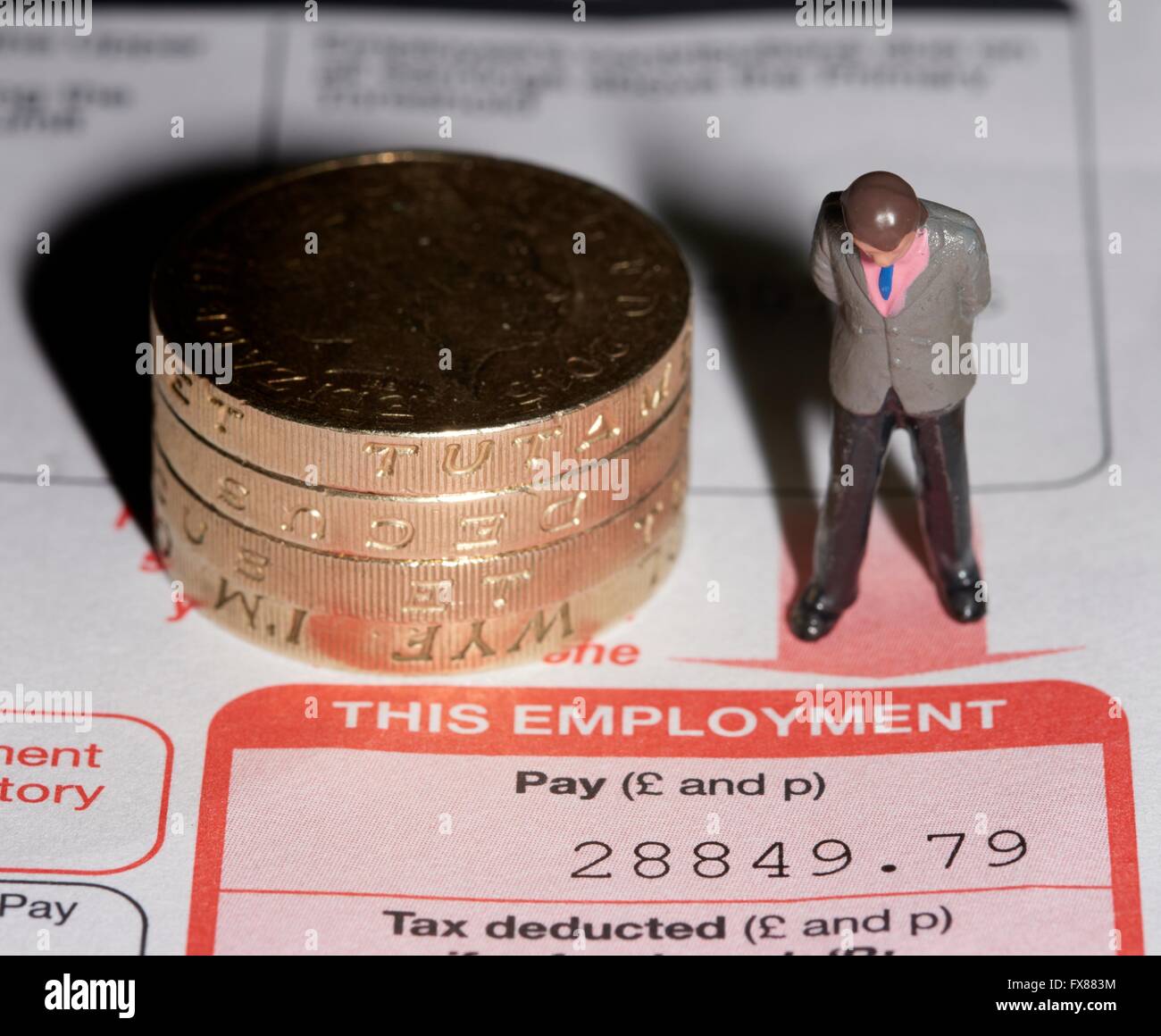 Una statuetta in miniatura uomo in piedi accanto a una pila di libbra di monete su una P60 di fine anno di certificato fiscale. Foto Stock