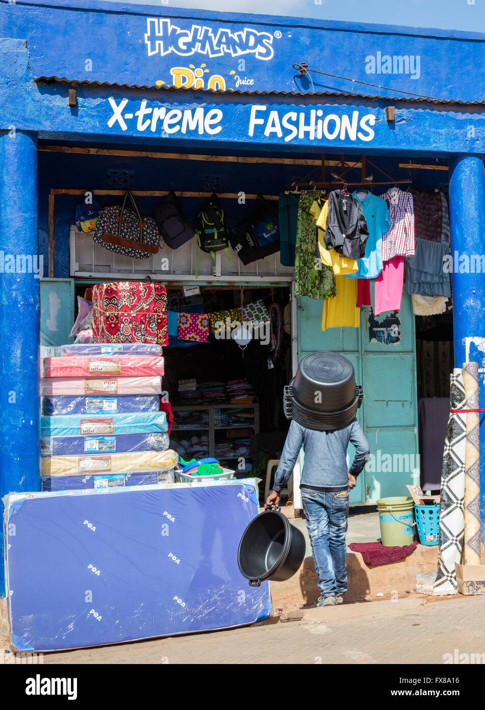 Un uomo che indossa una grande ciotola di polietilene come un cappello nel sole caldo al di fuori di un negozio di moda in Voi il Kenya meridionale Foto Stock