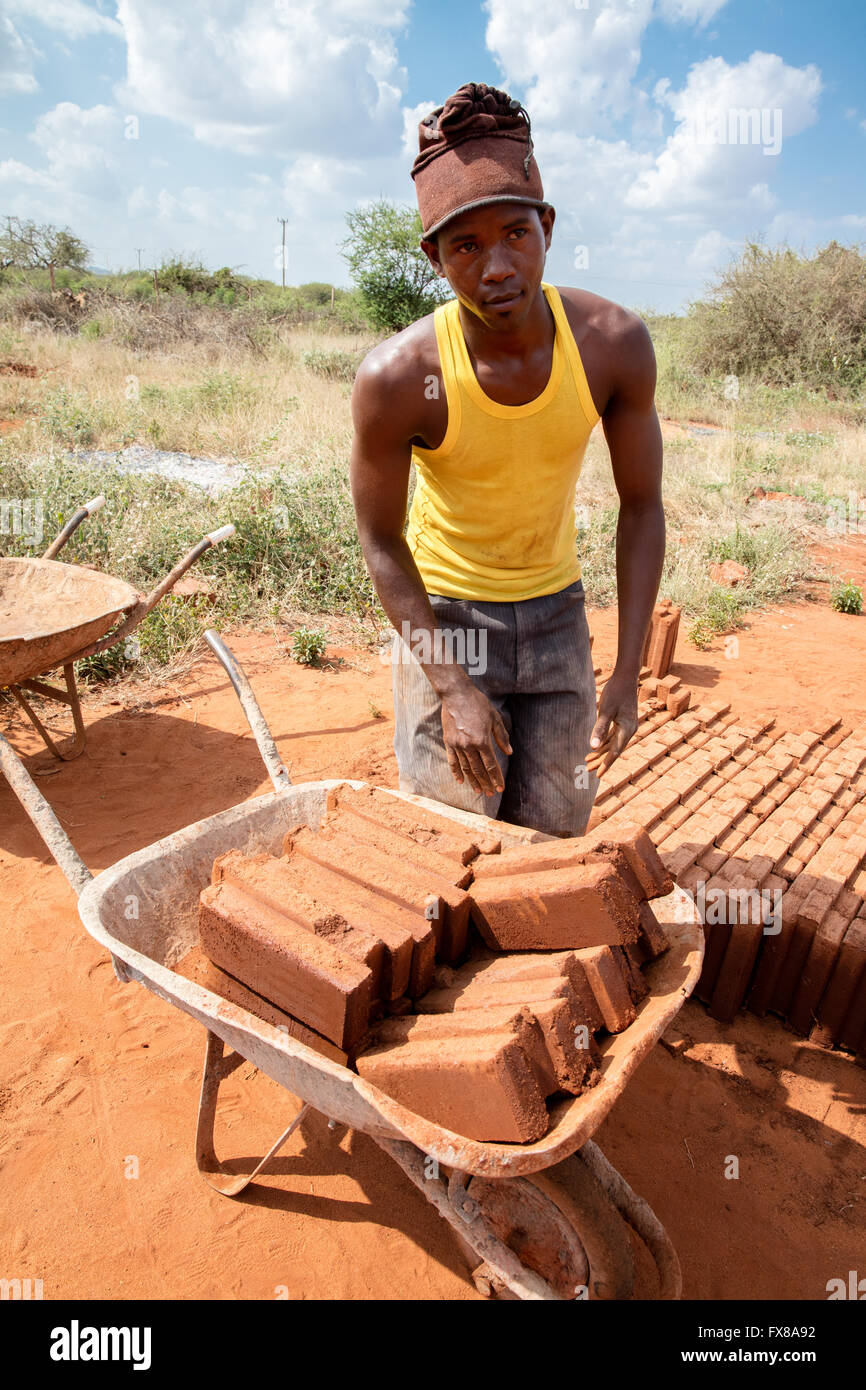 Uomo del Kenya con una carriola piena di fatto a mano mattoni su un edificio sito vicino a Voi Kenya Africa Foto Stock