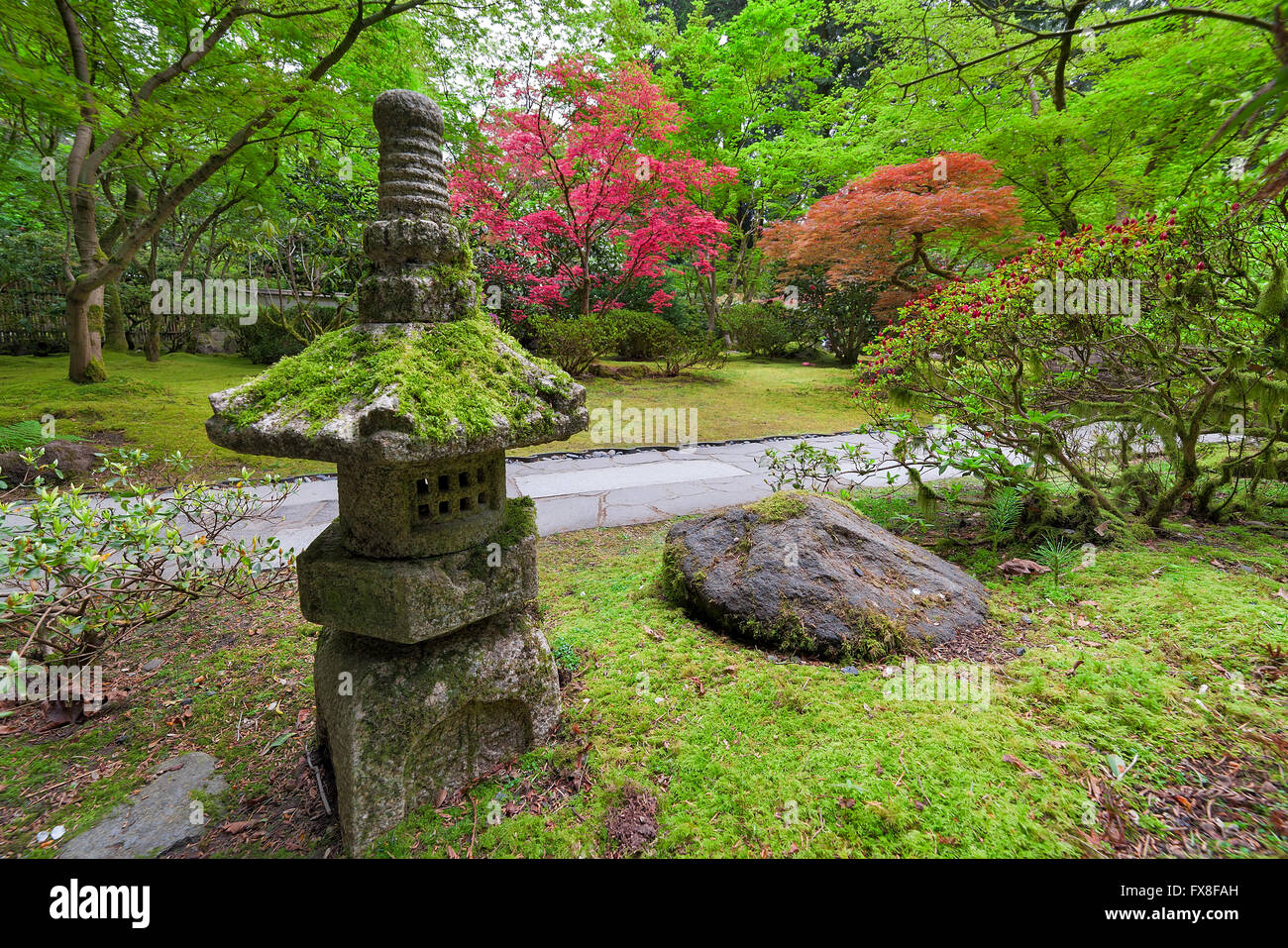 Vecchia lanterna di pietra nel giardino giapponese con arbusti e alberi paesaggio nella stagione primaverile Foto Stock