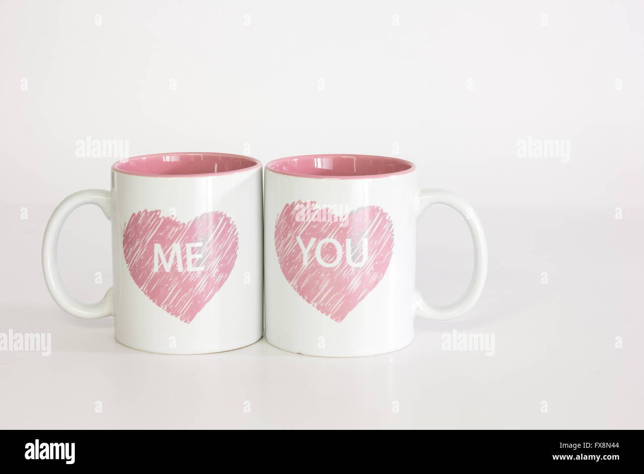 Bianco due tazze da caffè con un logo di cuore spinto insieme vicino l'ortografia 'me'. Isolati contro un puro sfondo bianco Foto Stock