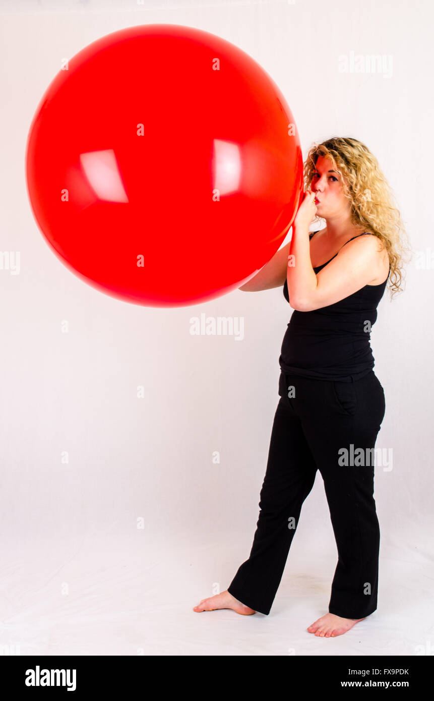 Giovane donna gonfiare un enorme pallone rosso per bocca Foto Stock