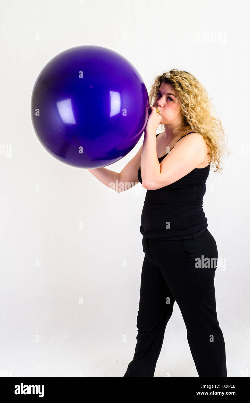 Giovane donna gonfiare un enorme pallone viola per bocca Foto Stock