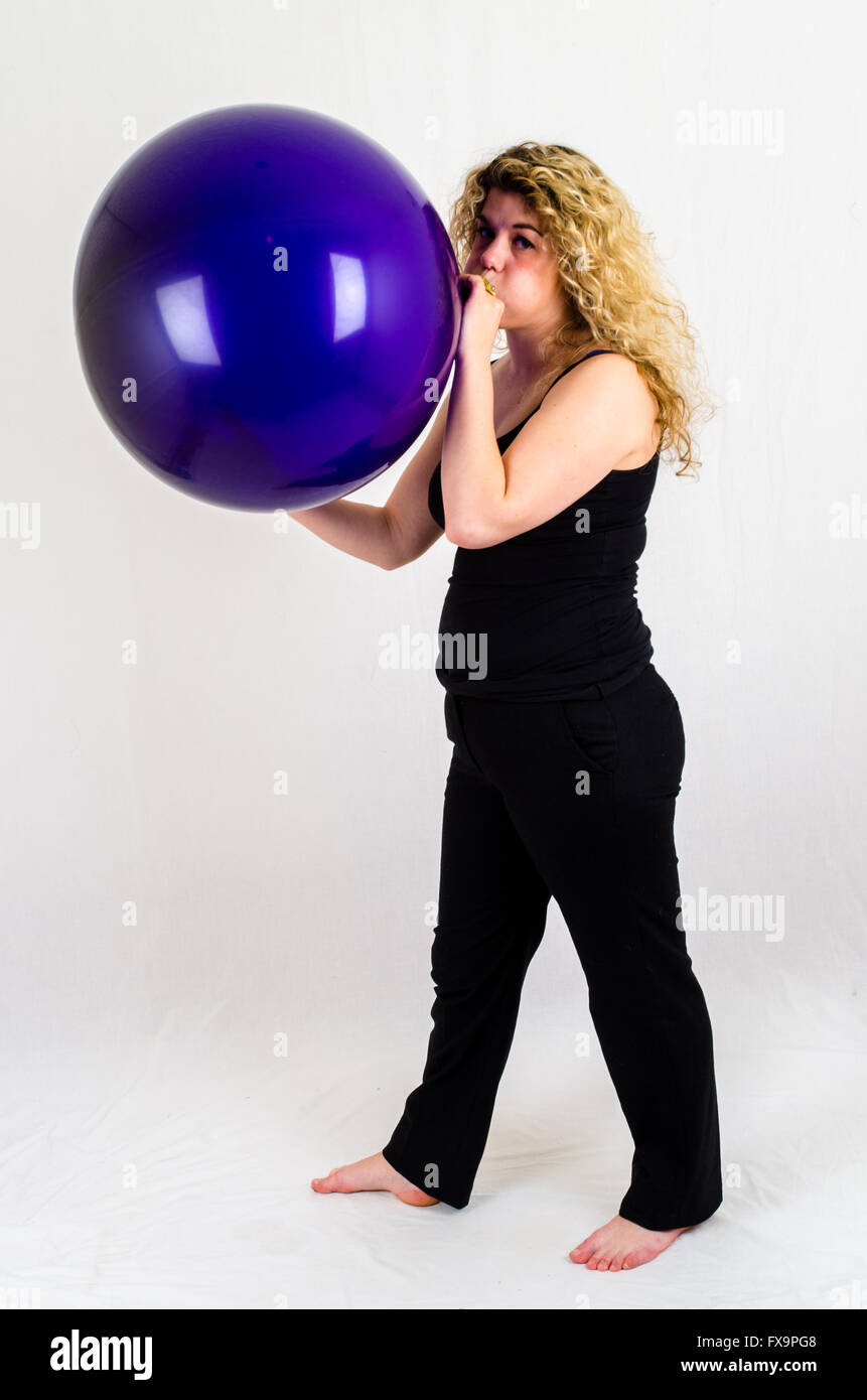 Giovane donna gonfiare un enorme pallone viola per bocca Foto Stock