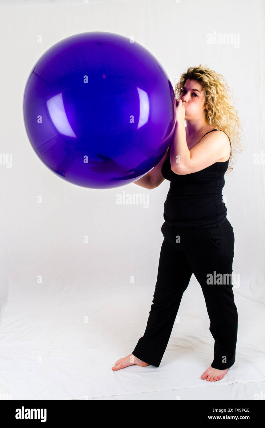 Giovane donna gonfiare un enorme pallone viola per bocca Foto Stock
