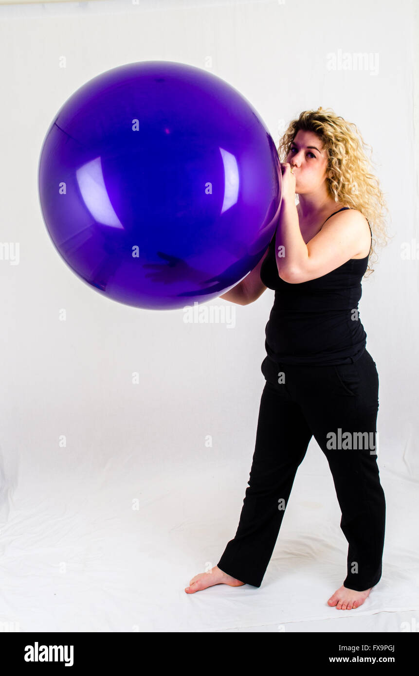 Giovane donna gonfiare un enorme pallone viola per bocca Foto Stock