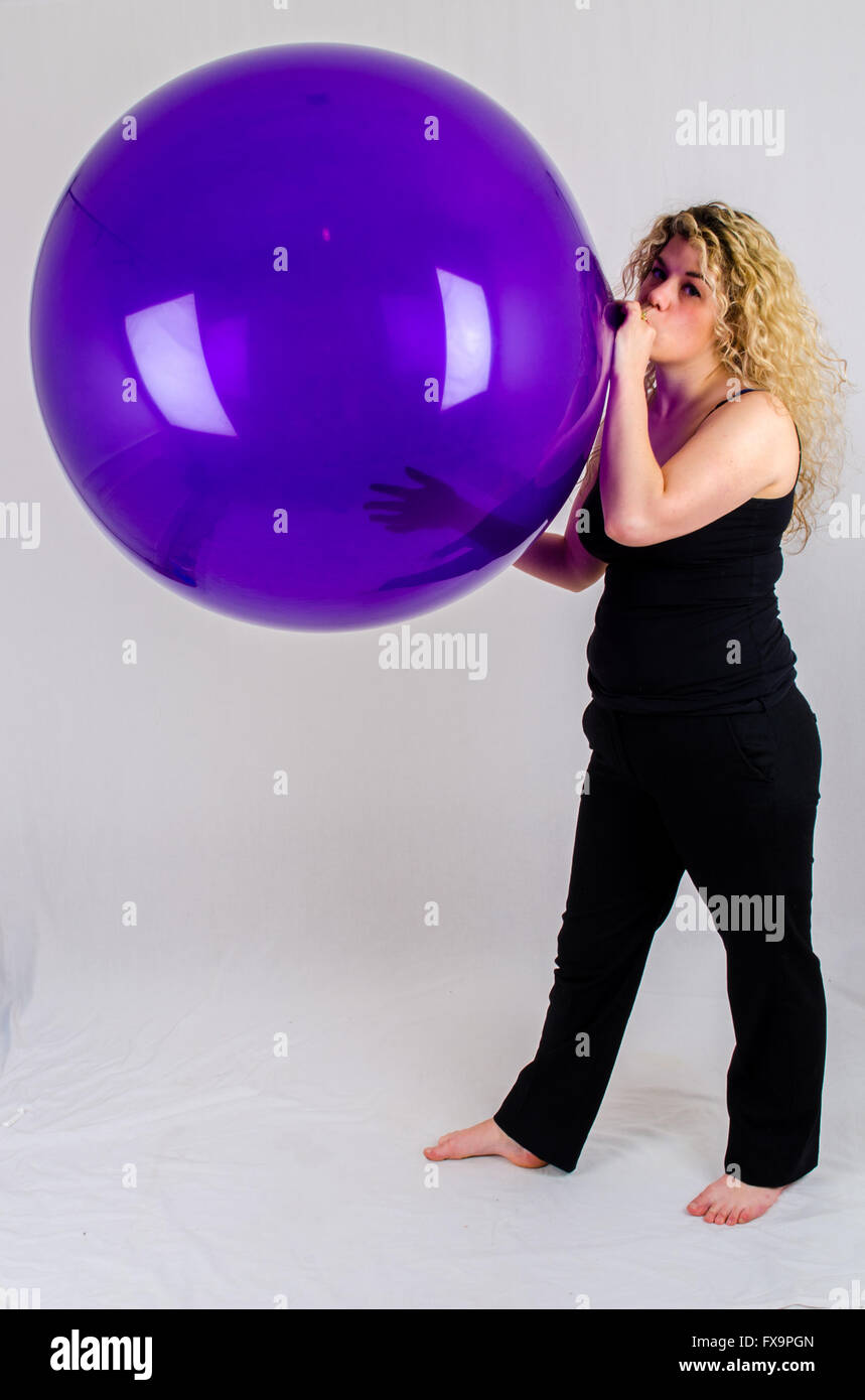 Giovane donna gonfiare un enorme pallone viola per bocca Foto Stock