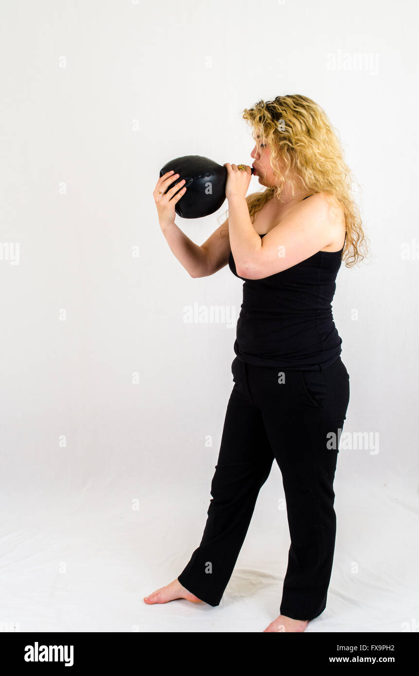 Giovane donna gonfiare un enorme pallone nero per bocca Foto Stock