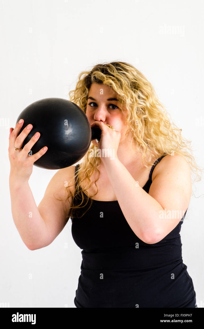 Giovane donna gonfiare un enorme pallone nero per bocca Foto Stock