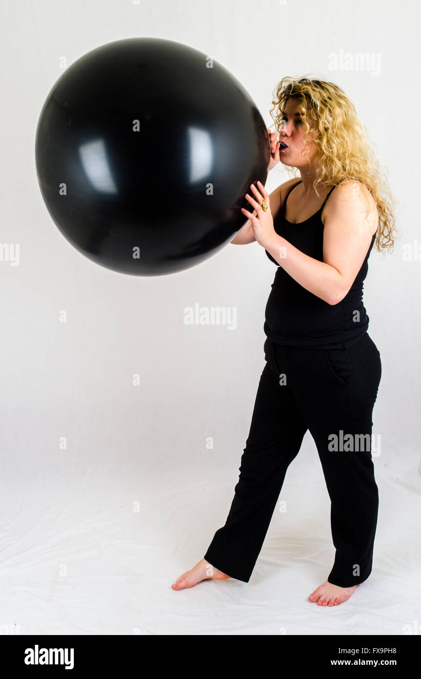 Giovane donna gonfiare un enorme pallone nero per bocca Foto Stock