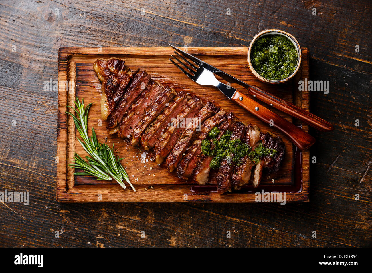 Fette di manzo alla griglia barbecue controfiletto di manzo con salsa chimichurri sul tagliere in legno scuro dello sfondo Foto Stock