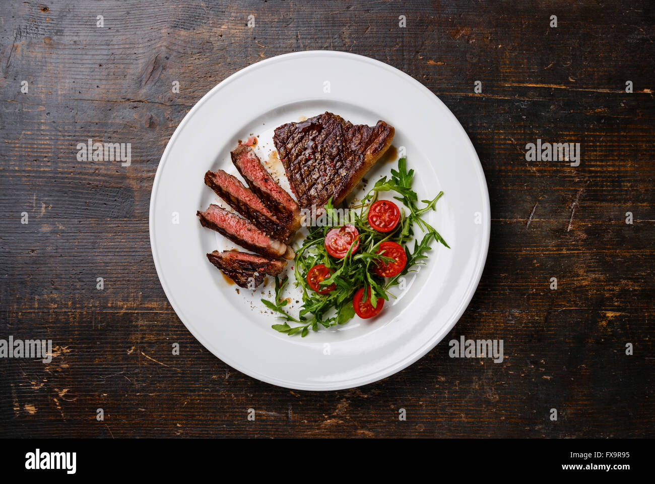 Fette di mezzo raro grigliate di carne di manzo del roastbeef con insalata e pomodori e rucola sulla piastra bianca su scuro dello sfondo in legno Foto Stock