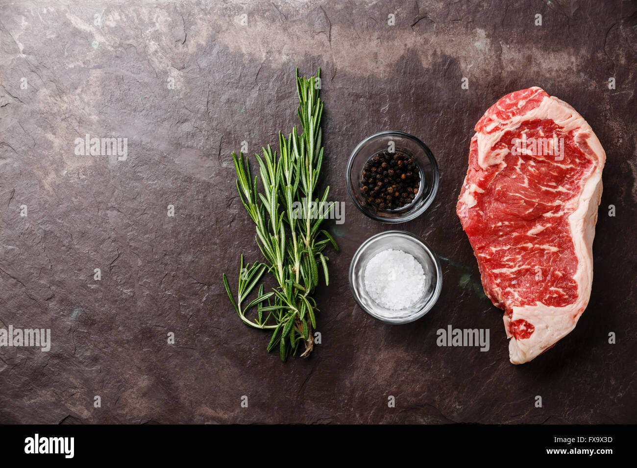 Materie carni fresche bistecca di controfiletto al rosmarino, sale e pepe in pietra sullo sfondo di ardesia Foto Stock