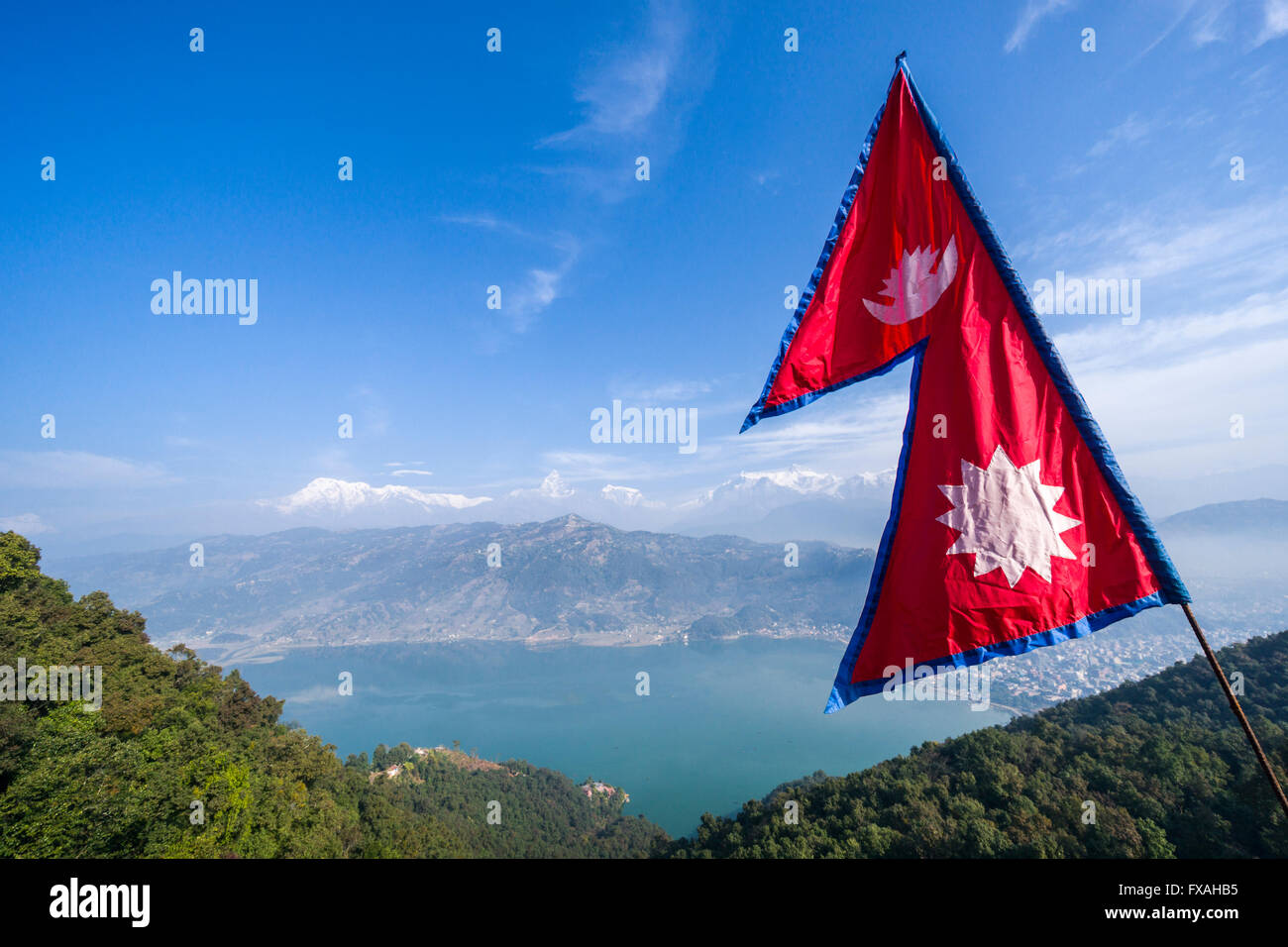 Il nepalese bandiera nazionale sventolando in alto sopra il lago Phewa e Pokhara, Annapurna montagne in distanza, Thumki, Kaski, Nepal Foto Stock