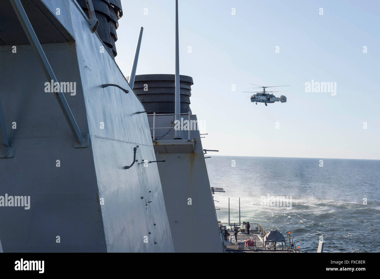 Un russo Kamov Ka-27 elicottero elica rende molto bassa altitudine passa al di sopra della U.S Navy Arleigh Burke-class guidato-missile destroyer USS Donald Cook durante una pattuglia Aprile 12, 2016 nel Mar Baltico. L'aggressiva manovre di volo dagli aerei Russi simulato un bombardamento esegui. Foto Stock