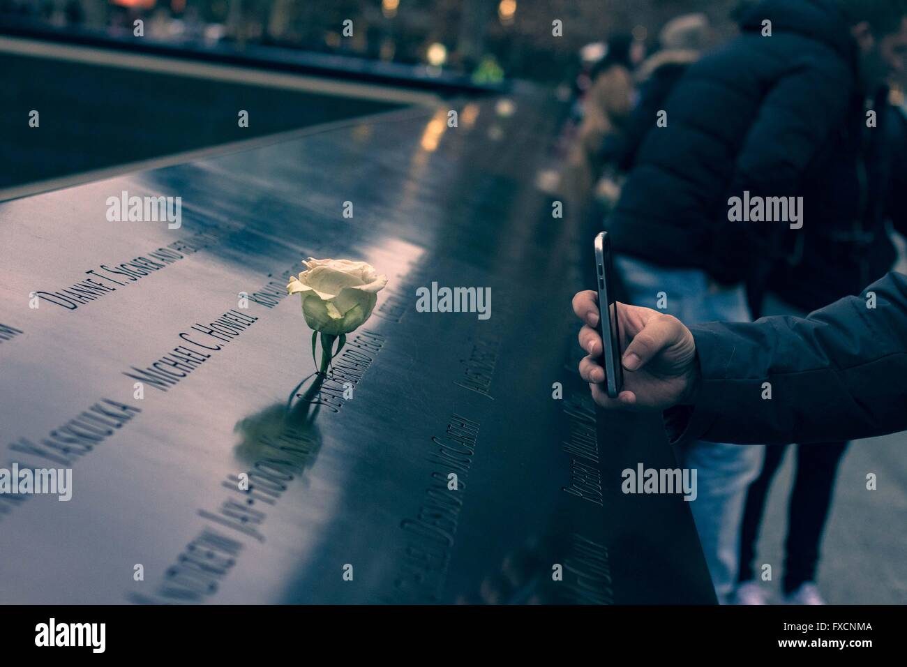 Un uomo prende una foto di un fiore al Ground Zero memorial a New York. Foto Stock