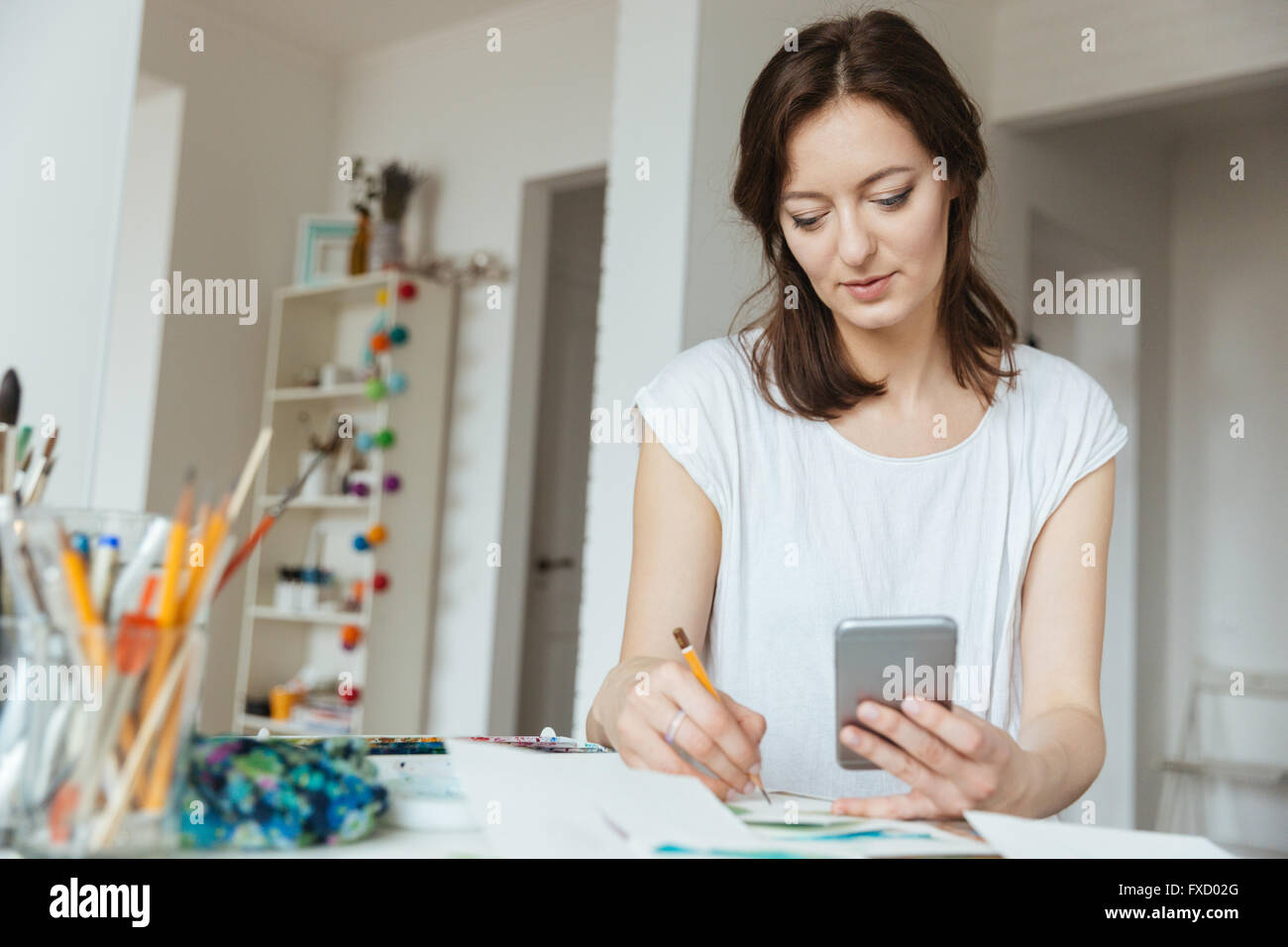 Concentrato di bella donna artista disegno e utilizza lo smartphone in officina Foto Stock