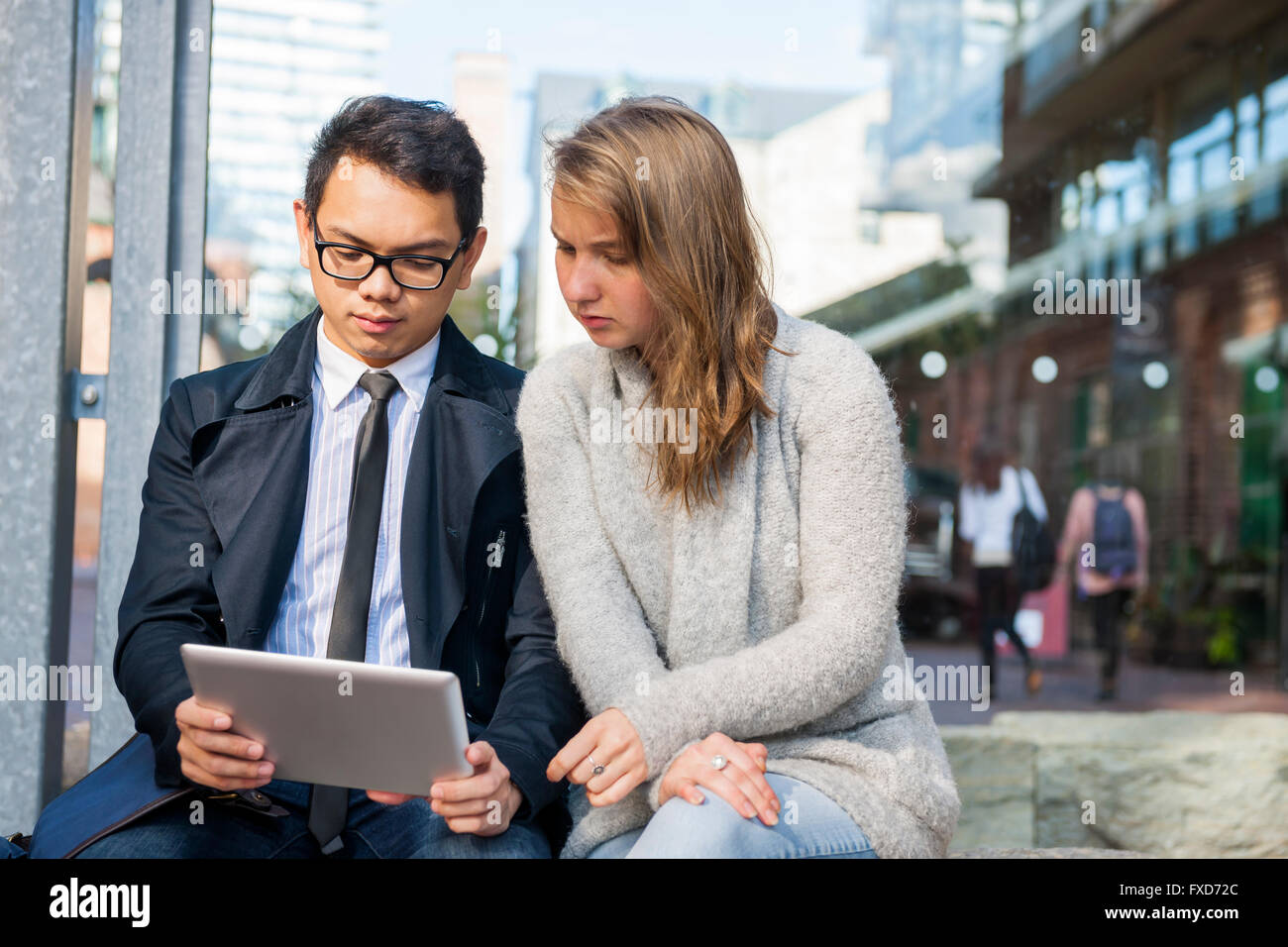 Due gravi giovani cercando in digitale compressa seduto fuori sulla strada di città Foto Stock