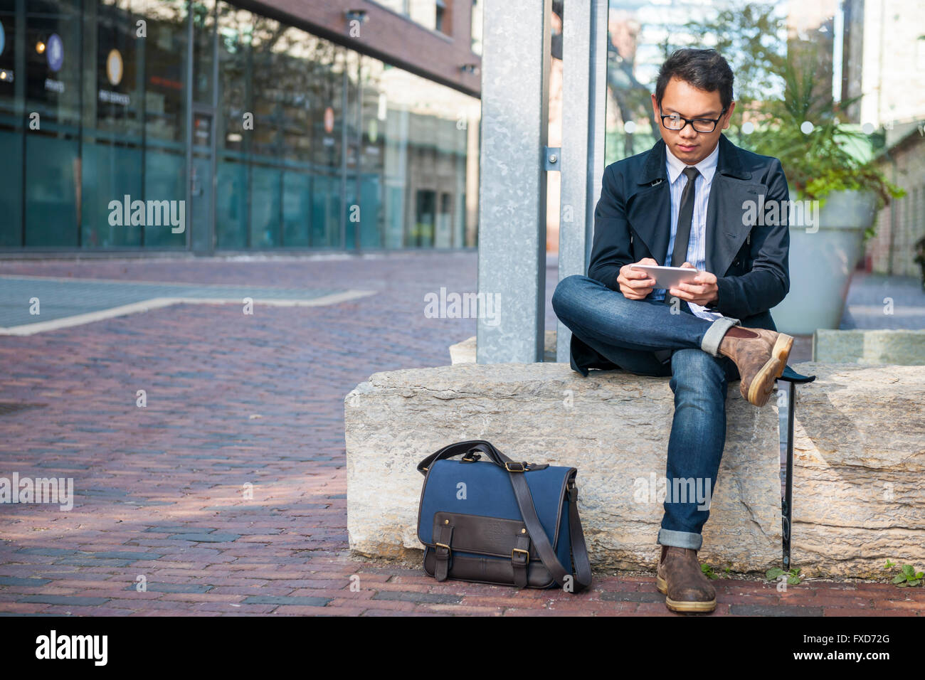Giovane grave Asian business un uomo guarda il telefono cellulare al di fuori seduta su una strada di città con lo spazio di copia Foto Stock