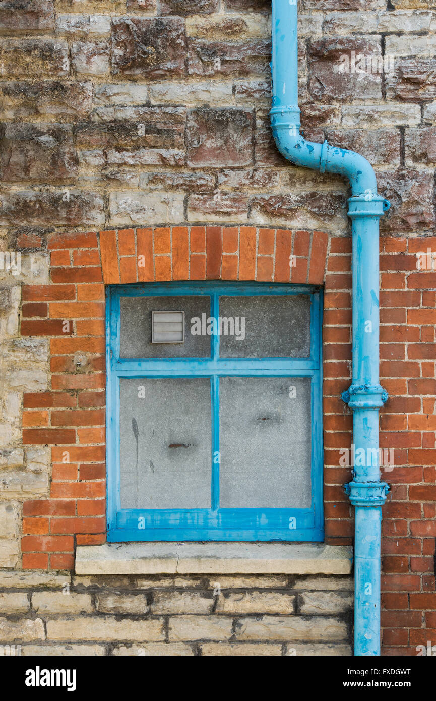 Pietra e mattoni casa parete con finestre blu e drainpipe astratta. Glastonbury, Somerset, Inghilterra Foto Stock