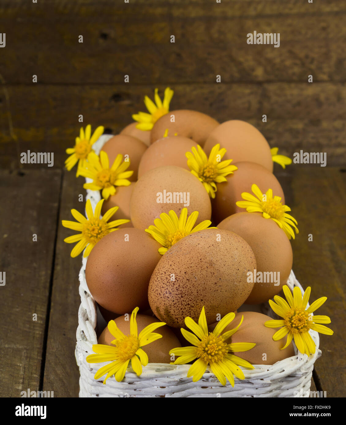 Foto di uova di gallina e daisy giallo dei fiori in un cesto su di un legno rustico sfondo Foto Stock