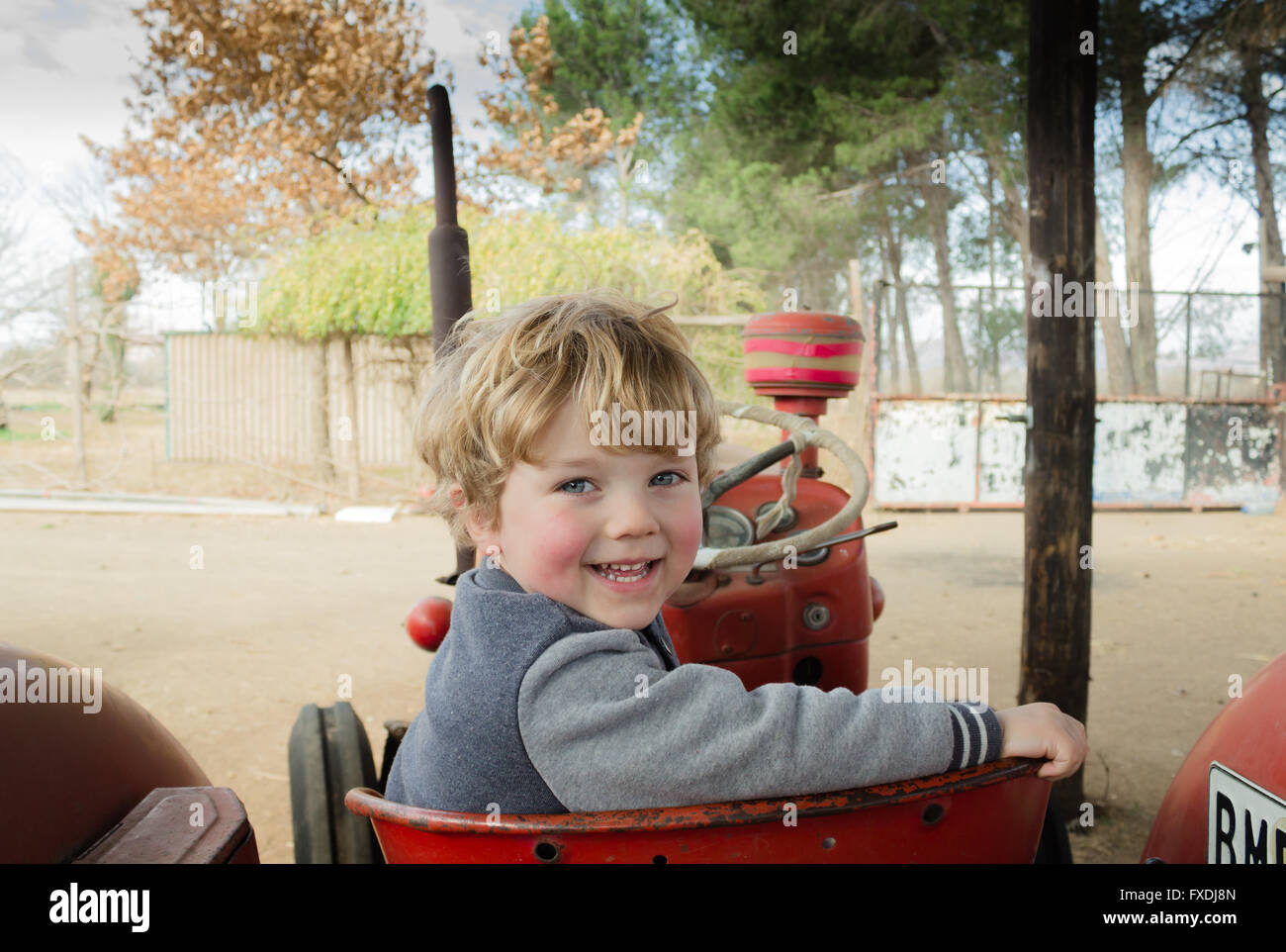 Sorridente tre anno vecchio ragazzo guardando sopra la spalla sul rosso trattore vintage Foto Stock